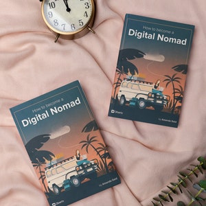 May include: Two copies of the book "How to become a Digital Nomad" by Amanda Gaid. The book cover features a cartoon illustration of a person working on a laptop in a van with palm trees in the background. The book is on a pink blanket with a gold alarm clock.
