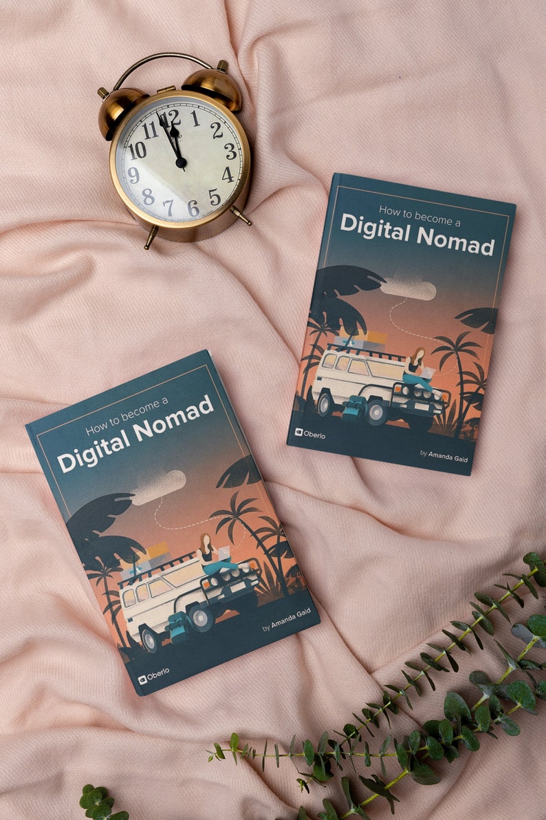 May include: Two copies of the book "How to become a Digital Nomad" by Amanda Gaid. The book cover features a cartoon illustration of a person working on a laptop in a van with palm trees in the background. The book is on a pink blanket with a gold alarm clock.