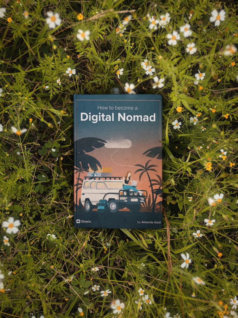 May include: A book titled "How to become a Digital Nomad" with an illustration of a person working on a laptop in a car. The book cover is blue with a sunset scene and palm trees.
