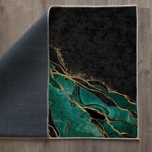 Puede incluir: Una alfombra de &aacute;rea abstracta verde y dorada con fondo negro. La alfombra tiene un dise&ntilde;o moderno y geom&eacute;trico con un patr&oacute;n de m&aacute;rmol.