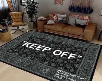 May include: A black and grey patterned rug with the text "KEEP OFF" in white lettering. The rug has a border with a floral design. The text "IKEA c/o Virgil Abloh" is printed in white at the bottom of the rug.