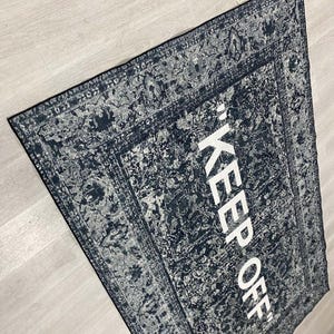 May include: A black and white rug with a vintage design and the text "KEEP OFF" in white lettering.