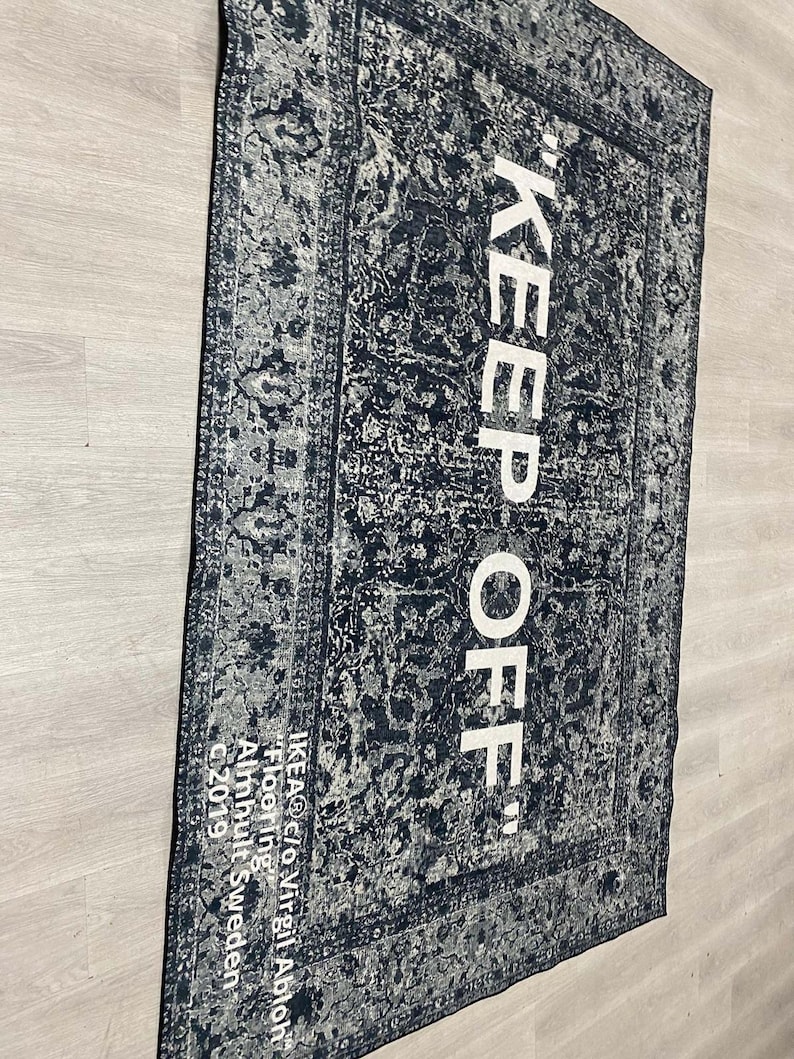 May include: Black and white rug with a vintage pattern and the text "KEEP OFF" in white. The rug is labeled "IKEA&reg; c/o Virgil Abloh" and "Flooring" in white text. The rug is made in Almhult, Sweden.