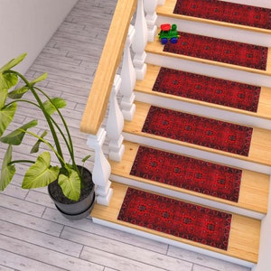 May include: Red patterned stair treads with a traditional design. The treads are placed on a wooden staircase with a white railing.