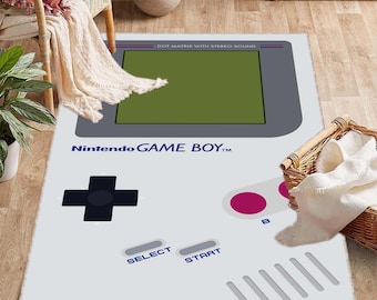 May include: A white and gray rug with a Game Boy design. The rug features a gray screen with the text "DOT MATRIX WITH STEREO SOUND" and "Nintendo GAME BOY TM". The rug also has a gray directional pad, two gray buttons, and a gray select and start button.