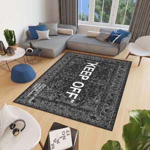 May include: A black and white area rug with a distressed vintage look. The rug has a white border and the text "KEEP OFF" in white lettering.