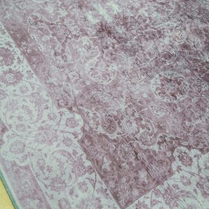 May include: A vintage-style rug with a faded floral pattern in shades of pink and white. The rug has a distressed look and a border with a more intricate design.