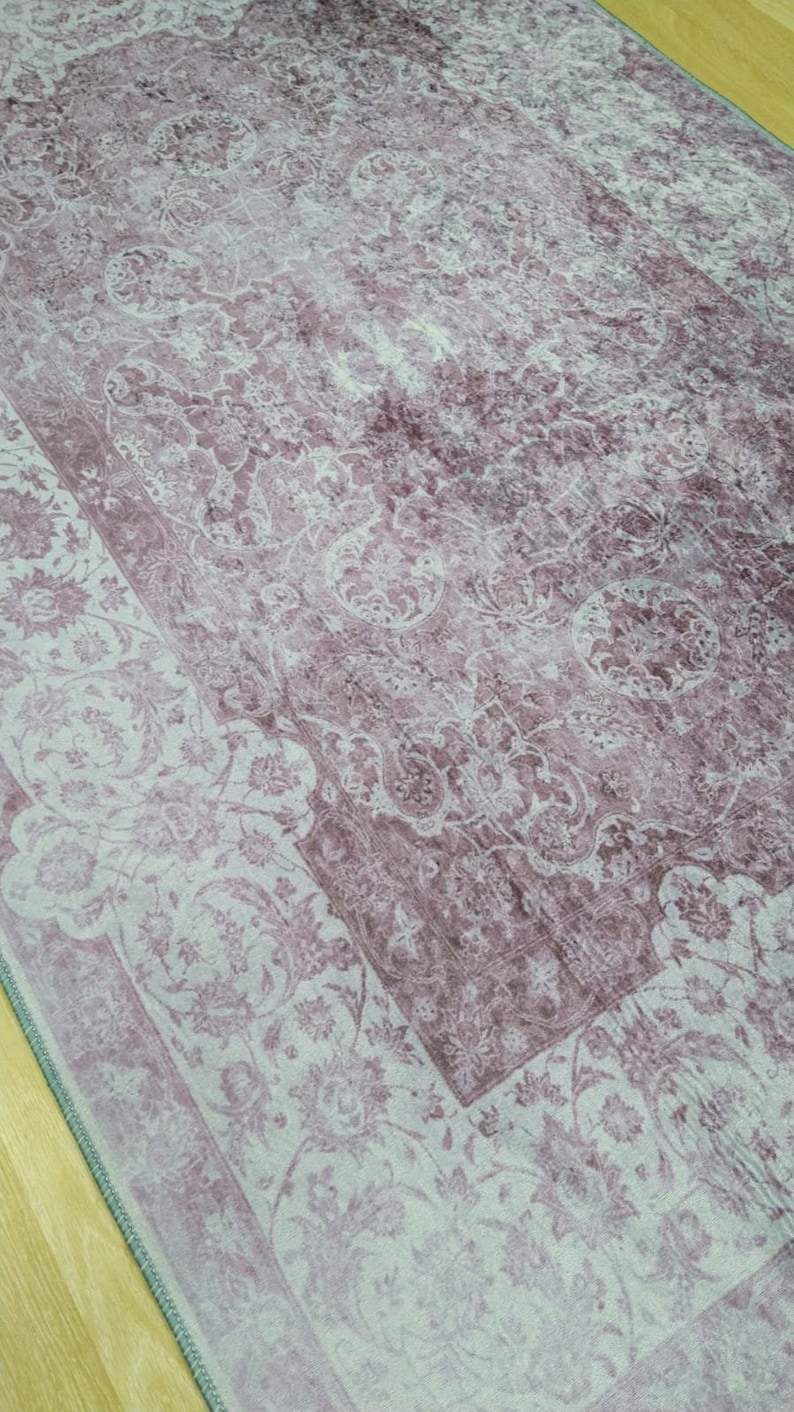 May include: A vintage-style rug with a faded floral pattern in shades of pink and white. The rug has a distressed look and a border with a more intricate design.