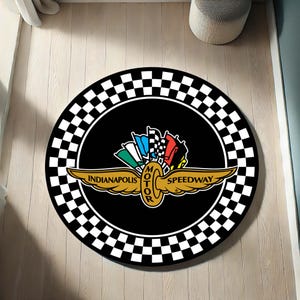 Puede incluir: Alfombra redonda negra con borde a cuadros blancos y negros. El centro presenta el logotipo de Indianapolis Motor Speedway con un emblema dorado y banderas coloridas. Diseñada para uso en interiores.