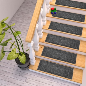 May include: A set of six grey patterned non-slip stair treads. The treads are placed on wooden stairs with a white railing.