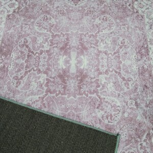 May include: A pink and white patterned rug with a dark brown backing. The rug has a floral design with a central medallion.
