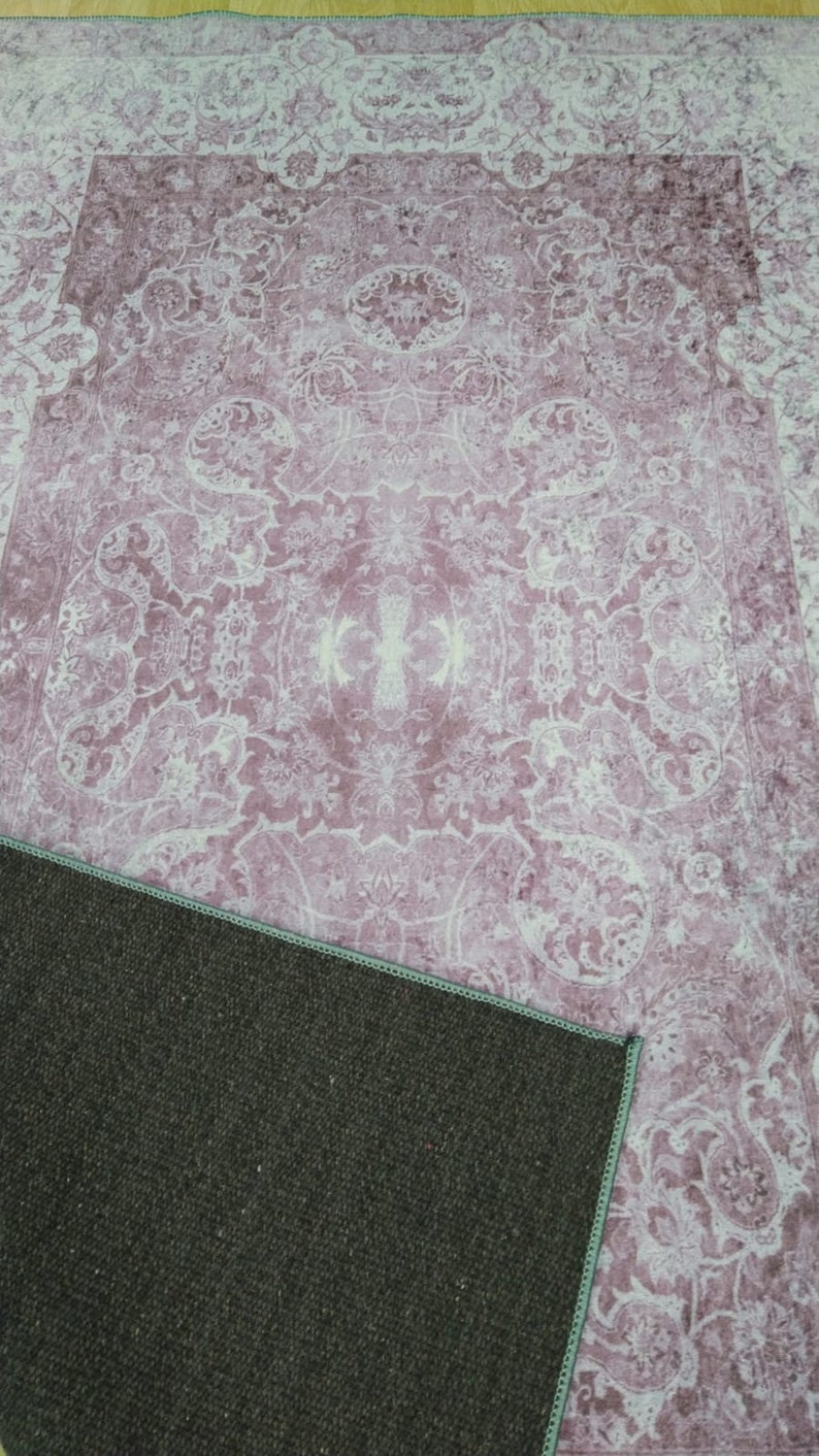 May include: A pink and white patterned rug with a dark brown backing. The rug has a floral design with a central medallion.
