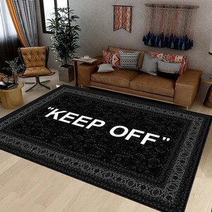 Könnte beinhalten: Schwarz-weißer Teppich mit einem Vintage-Blumenmuster und einem weißen Rand. Der Teppich trägt den Schriftzug "KEEP OFF" in weißen Buchstaben.