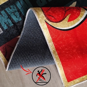 K&ouml;nnte beinhalten: Nahaufnahme der R&uuml;ckseite eines roten, goldenen und schwarzen Teppichs mit rutschfester Unterseite. Der Teppich hat ein grafisches Design mit einem stilisierten Spinnennetz. Der Text "Spider-Man" ist auf dem Teppich sichtbar.