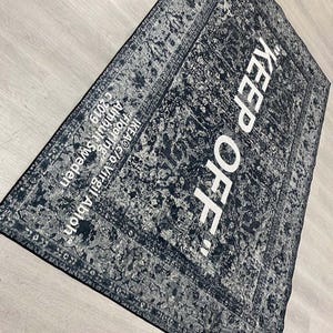 May include: Black and white rug with a distressed pattern and the text "KEEP OFF!" in white.