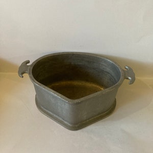 May include: A gray cast iron triangular baking dish with two handles. The dish is empty and has a smooth, slightly textured surface.