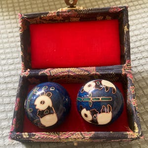 May include: Two spherical metal balls with a deep blue enamel finish featuring white and black panda bear designs and green bamboo stalks, housed in a rectangular fabric-covered box with a red interior lining and a gold-toned metal latch.