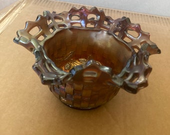 May include: A small, iridescent glass bowl with a woven basket design. The bowl has a scalloped edge and is made in a dark purple, blue, and gold color.