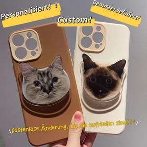 Könnte beinhalten: Zwei individuelle Handyhüllen mit Katzen-Gesichtern. Eine Hülle ist braun, die andere cremefarben. Die Hüllen haben einen transparenten, kreisförmigen Griff mit einem aufgedruckten Katzen-Gesicht. Text: "Custom!" und "Personalisiert!"