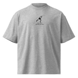 May include: A heather gray t-shirt with a mock neck and short sleeves. The shirt features a black graphic of a tennis player and the text "THE BOY FROM BLYTH" in black. The shirt has a relaxed fit.