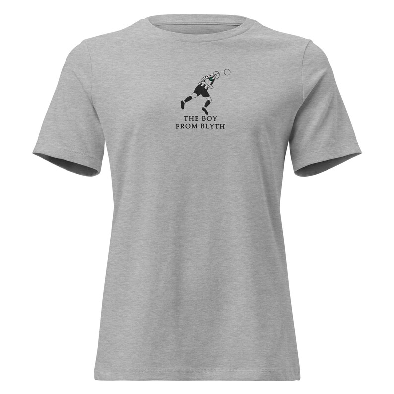 May include: A grey t-shirt with a black and white illustration of a footballer kicking a ball. The text "THE BOY FROM BLYTH" is printed beneath the image. The shirt has a crew neck and short sleeves.