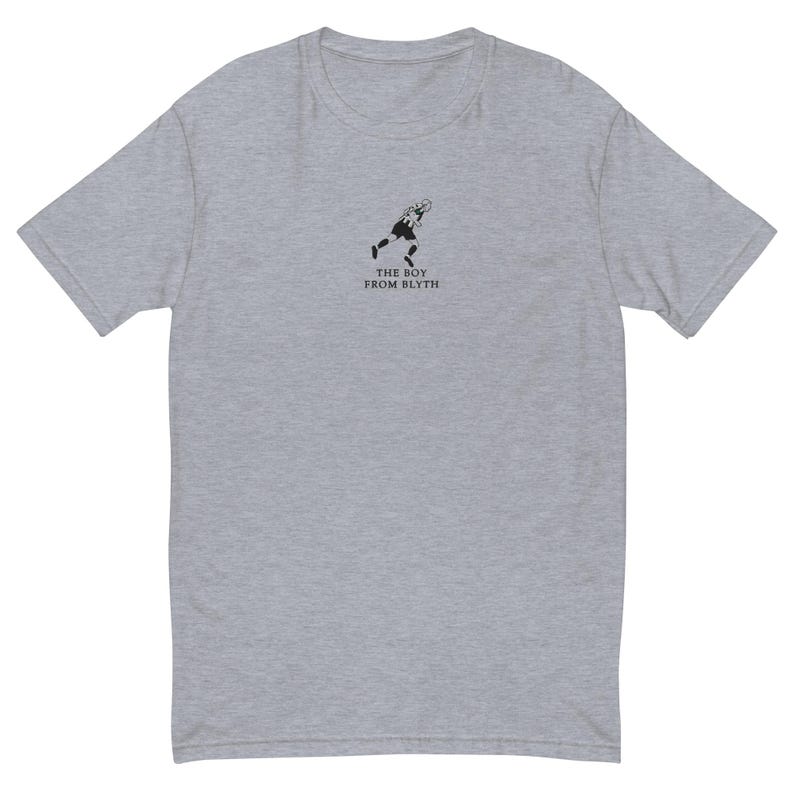 K&ouml;nnte beinhalten: Hellgraues T-Shirt mit einer kleinen schwarzen Grafik einer rennenden Person und dem Text "THE BOY FROM BLYTH" darunter. Das T-Shirt hat kurze &Auml;rmel und einen Rundhalsausschnitt.