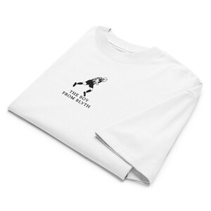 May include: White t-shirt with a black and white graphic of a person in athletic wear. The text "THE BOY FROM BLYTH" is printed below the graphic. The shirt is folded.