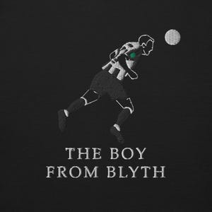 K&ouml;nnte beinhalten: Schwarz-wei&szlig; gesticktes Design eines Fu&szlig;ballspielers, der einen Ball k&ouml;pft. Der Text "THE BOY FROM BLYTH" ist darunter gestickt. Das Design befindet sich auf schwarzem Hintergrund.