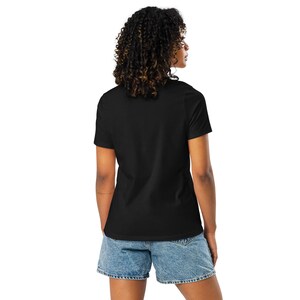 May include: A plain black t-shirt with short sleeves and denim shorts. The shorts are light blue and have a classic design. The person is seen from the back, with curly hair and wearing the casual outfit.