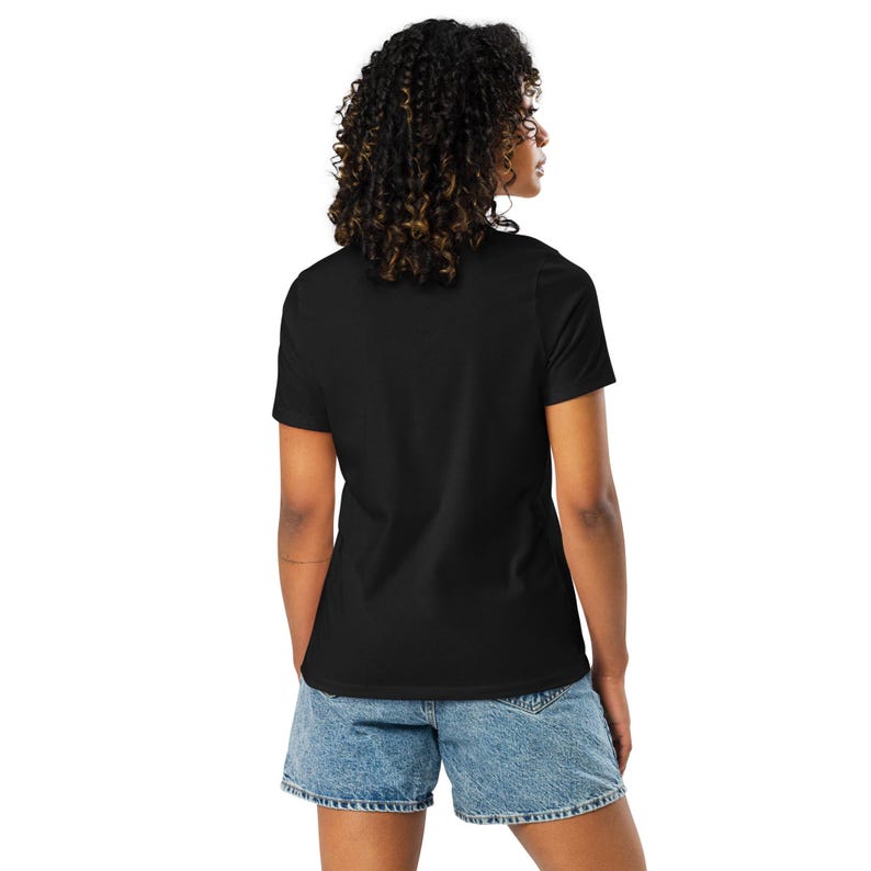 May include: A plain black t-shirt with short sleeves and denim shorts. The shorts are light blue and have a classic design. The person is seen from the back, with curly hair and wearing the casual outfit.