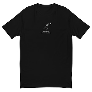 May include: Black t-shirt featuring a small, white graphic of a football player throwing a ball. Below the graphic is the text "THE BOY FROM BLYTH" in white. The shirt has short sleeves and a crew neck.