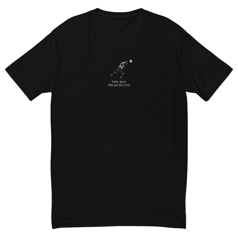 May include: Black t-shirt featuring a small, white graphic of a football player throwing a ball. Below the graphic is the text "THE BOY FROM BLYTH" in white. The shirt has short sleeves and a crew neck.