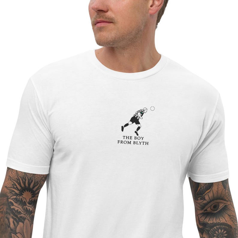 K&ouml;nnte beinhalten: Wei&szlig;es T-Shirt mit einer Schwarz-Wei&szlig;-Illustration eines Fu&szlig;ballspielers, der einen Ball tritt. Der Text "THE BOY FROM BLYTH" ist unter der Illustration aufgedruckt. Das Shirt ist aus weichem Material.