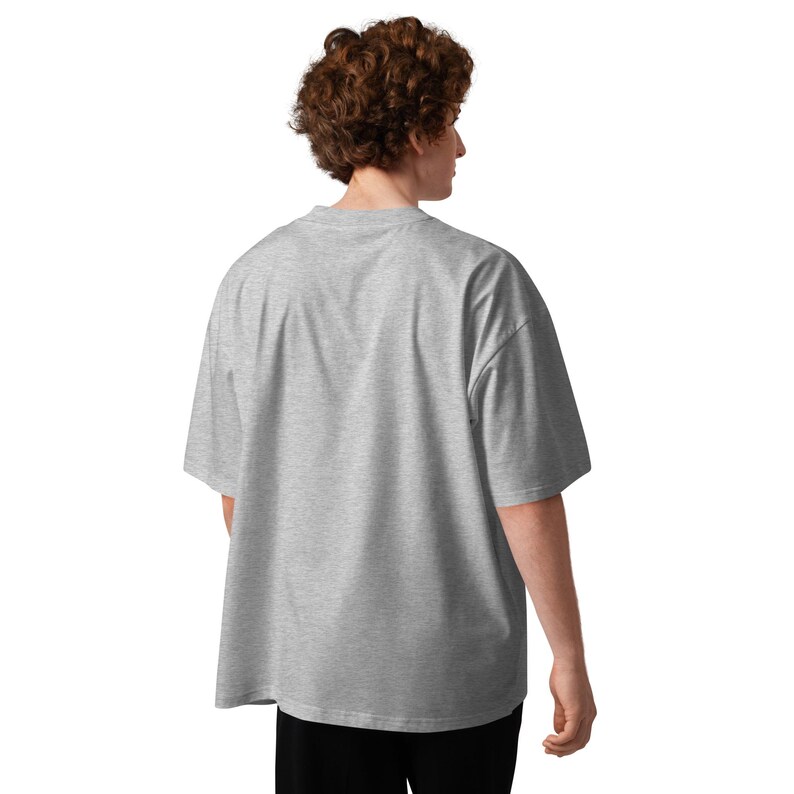 May include: A light gray, oversized t-shirt with short sleeves. The shirt is made of a soft, comfortable material and has a relaxed fit. The model is wearing black pants. The back of the shirt is visible.