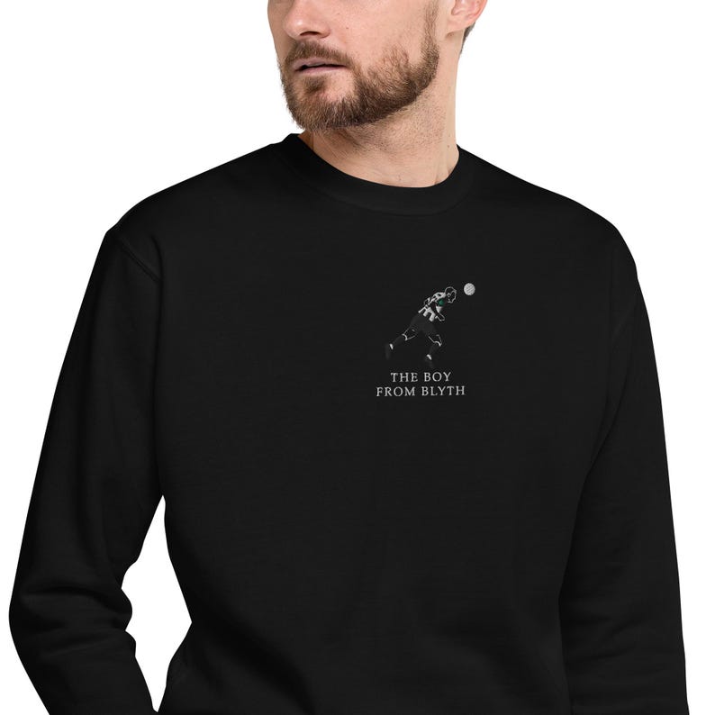 K&ouml;nnte beinhalten: Schwarzes Sweatshirt mit einer kleinen wei&szlig;en Grafik eines Footballspielers, der einen Ball wirft. Der Text "THE BOY FROM BLYTH" ist darunter gedruckt. Das Sweatshirt ist aus einem weichen Material.
