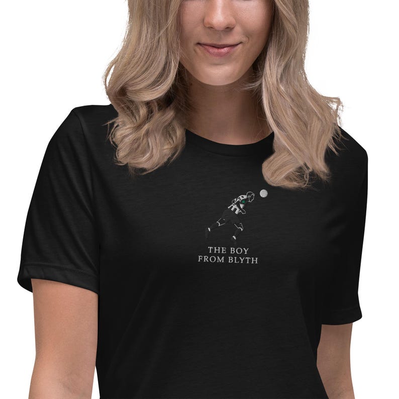 K&ouml;nnte beinhalten: Schwarzes T-Shirt mit einer minimalistischen Illustration eines Fu&szlig;ballspielers, der einen Ball tritt. Der Text "THE BOY FROM BLYTH" ist darunter gedruckt. Das T-Shirt ist aus weichem Material.