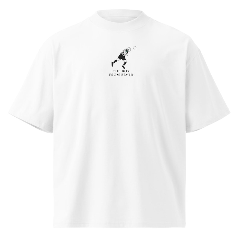 May include: White t-shirt with a mock neck and short sleeves. The shirt features a black and white graphic of a soccer player kicking a ball, with the text "THE BOY FROM BLYTH" below the graphic.