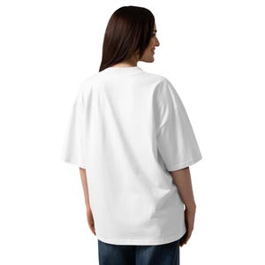May include: A white, oversized t-shirt with short sleeves. The shirt is made of a soft material and has a relaxed fit. The model is wearing blue jeans. The shirt is a basic wardrobe staple.