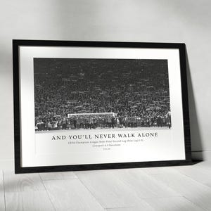 Puede incluir: Impresión enmarcada en negro con una fotografía en blanco y negro de un equipo de fútbol y una multitud. El texto "AND YOU'LL NEVER WALK ALONE" está en la parte inferior, junto con los detalles del juego. La impresión se muestra en una pared blanca.