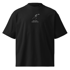 May include: Black short-sleeved t-shirt with a high neckline. The shirt features a white graphic of a person kicking a ball, with the text "THE BOY FROM BLYTH" below the graphic. The shirt has a relaxed fit.
