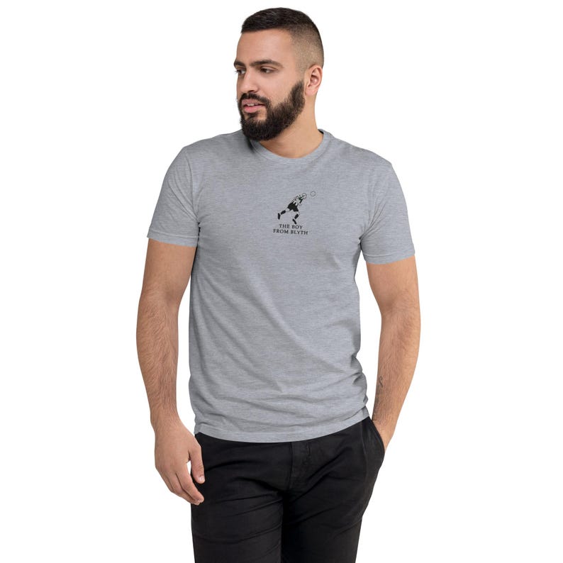 K&ouml;nnte beinhalten: Ein hellgraues T-Shirt mit einem schwarzen Aufdruck eines Tennisspielers und dem Text "THE BOY FROM BLYTH". Das kurz&auml;rmelige Oberteil hat einen Rundhalsausschnitt. Das T-Shirt ist aus weichem Material.