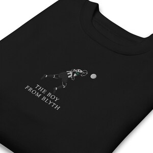 K&ouml;nnte beinhalten: Schwarzes Sweatshirt mit gesticktem Fu&szlig;ballspieler-Design. Der Text "THE BOY FROM BLYTH" ist in Wei&szlig; gestickt. Der Spieler tr&auml;gt ein schwarz-wei&szlig;es Trikot mit gr&uuml;nen Akzenten beim Schie&szlig;en.