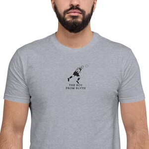 K&ouml;nnte beinhalten: Hellgraues T-Shirt mit einer minimalistischen schwarz-wei&szlig;en Illustration einer Person beim Sport und dem Text "THE BOY FROM BLYTH" darunter.