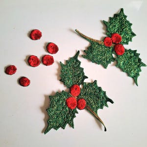 May include: Two embroidered holly leaf patches featuring dark green leaves with gold metallic thread detailing and three bright red circular berries on each. Six additional small, separate red circular embroidered berry patches are included.