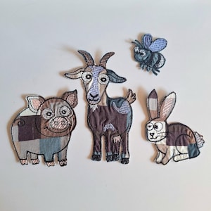Puede incluir: Cuatro parches de tela bordados que representan un cerdo, una cabra, un conejo y una abeja. Cada animal está construido con un mosaico de cuadrados de tela marrón, azul y crema con contornos cosidos en negro y ojos de estilo caricatura.