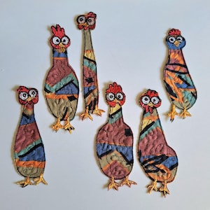 May include: Six embroidered chicken patches featuring a colourful abstract pattern of red, blue, orange, and tan sections. Each patch has a red comb, wide white eyes with black pupils, and yellow feet, all outlined in black thread stitching.