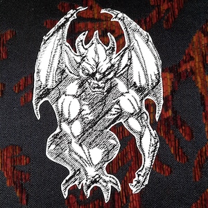 May include: A white patch featuring a black ink-style illustration of a winged gargoyle with horns and sharp claws. The creature is depicted in a crouching position with its wings spread upward, showcasing detailed cross-hatching and line work.