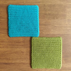 May include: Two square crochet coasters. One is turquoise, the other is green. The coasters are made with a tight stitch pattern and have a defined border. They are placed on a wooden surface.