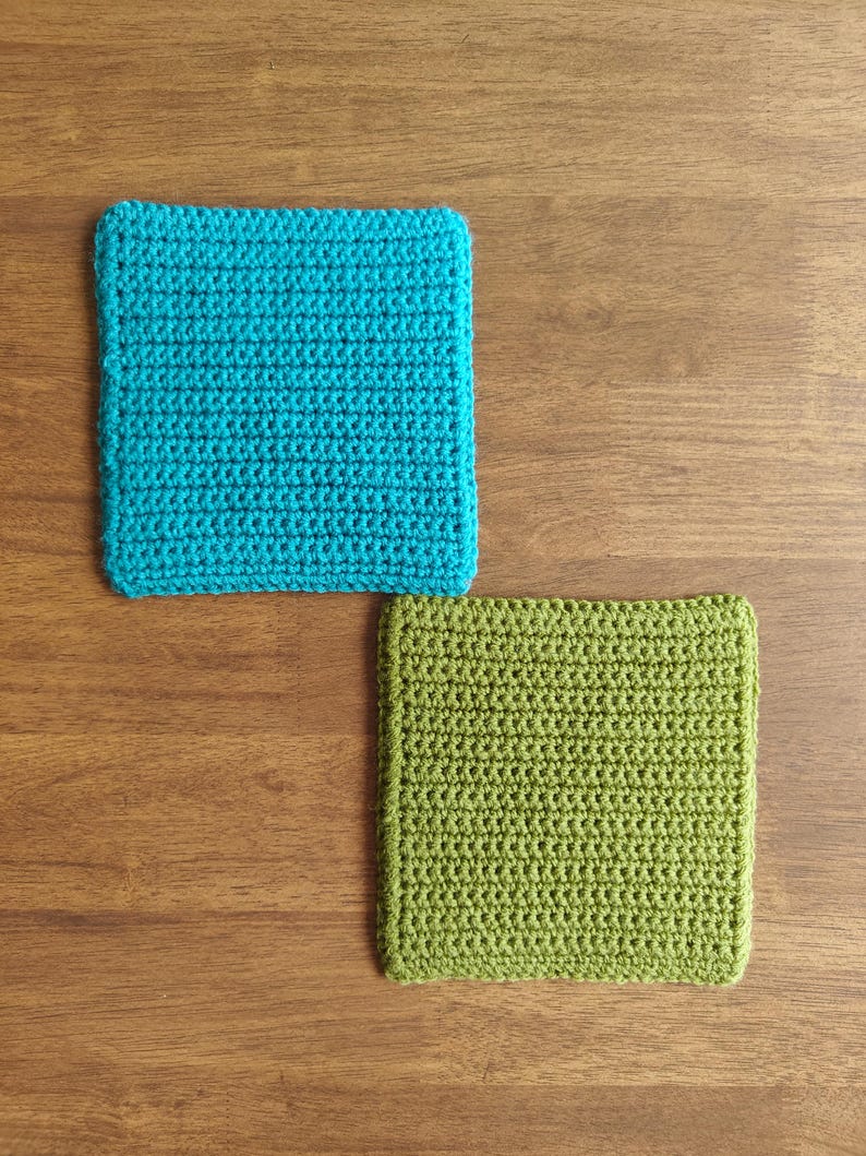 May include: Two square crochet coasters. One is turquoise, the other is green. The coasters are made with a tight stitch pattern and have a defined border. They are placed on a wooden surface.