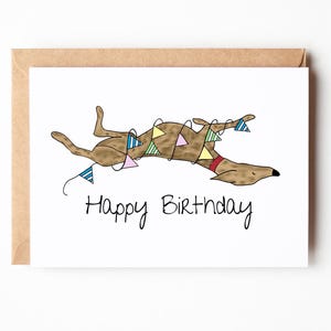 May include: A greeting card with a brown dog illustration, wearing a red collar and festive bunting. The words "Happy Birthday" are written in black script below the dog. The card is inside a brown envelope.
